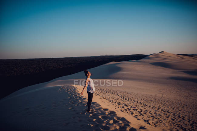Mujer alegre de pie en la duna de arena y disfrutando del sol . - foto de stock