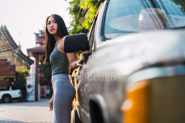 Jovem mulher apoiando-se no carro e olhando para longe — Fotografia de Stock