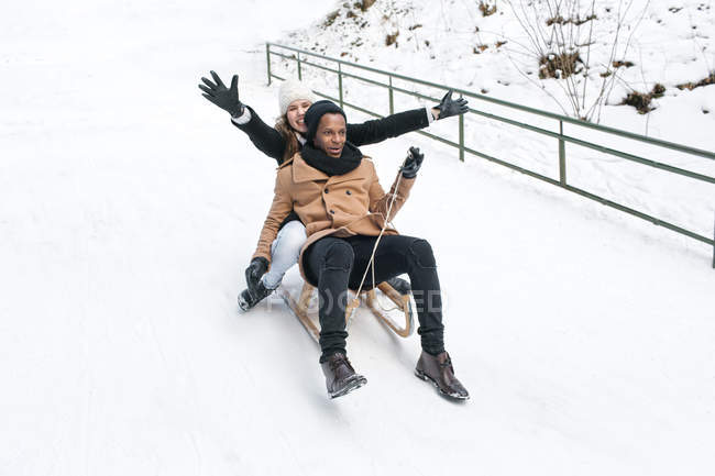 Pareja feliz montando trineo en la colina nevada - foto de stock