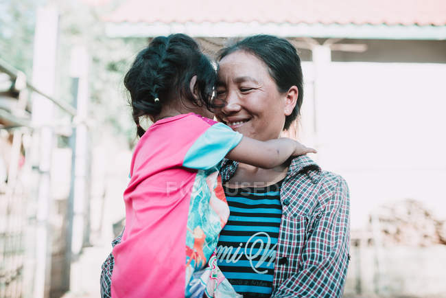 Nong khiaw, laos: lächelnde Frau umarmt kleines Mädchen auf Dorfstraße. — Stockfoto