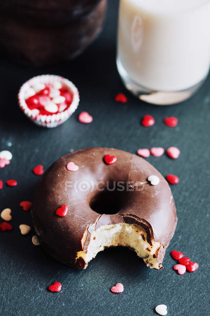 Bitten chocolate donut with toppings by glass of milk — Stock Photo