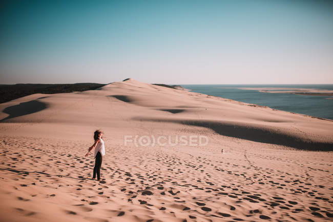 Vista lateral da mulher em pé na areia e desfrutar do sol . — Fotografia de Stock