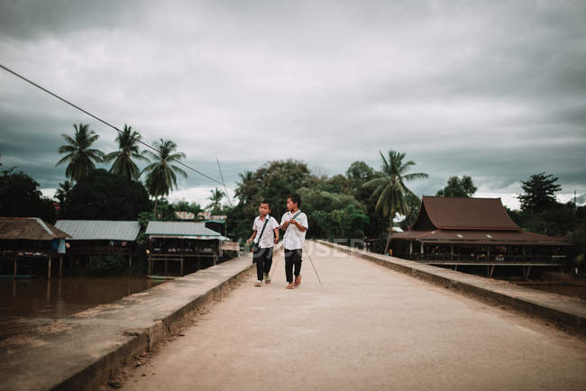 Laos, 4000 Inseln: Zwei Jungen in Schuluniform überqueren Zementbrücke. — Stockfoto