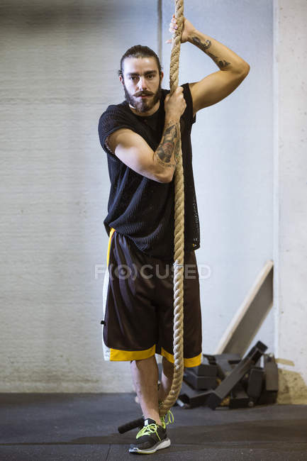 Hombre deportivo sosteniendo la cuerda en el gimnasio y mirando a la cámara - foto de stock