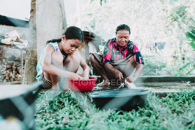 NONG KHIAW, LAOS: Niña y mujer adulta sentadas y haciendo tareas domésticas juntas . - foto de stock