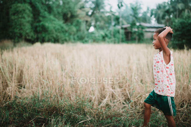 Лаос, 4000 острови область: Стороні подання хлопчика в повсякденний одяг, ходити в сухому поля. — стокове фото