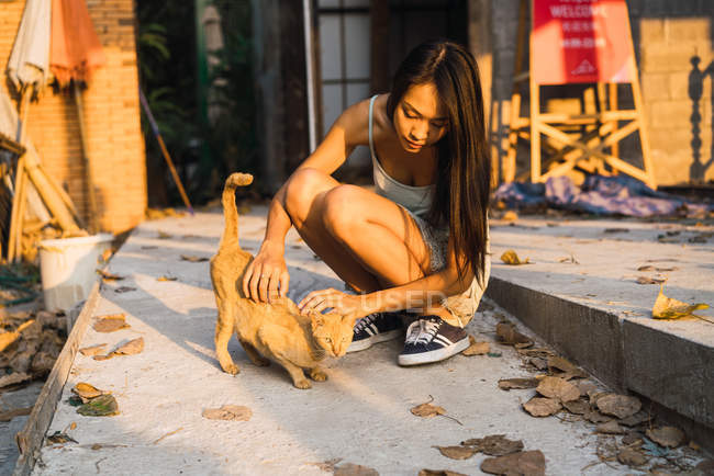 Yong woman playing with pale cat at street — Stock Photo