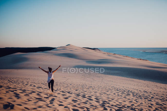 Rear view of woman running on sand with arms raised up — Stock Photo