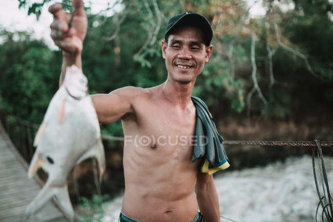 LAOS, 4000 ISLANDS AREA: Shirtless man demonstrating fish and smiling — Stock Photo