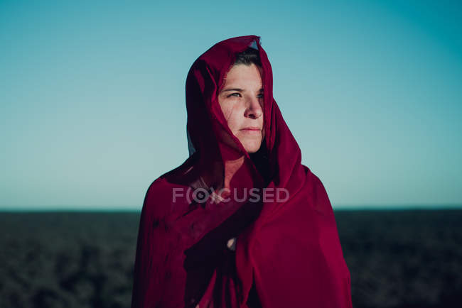 Portrait  woman wrapped in red fabric standing on sand and looking away — Stock Photo