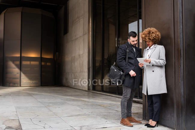 Stylish adult man and woman standing at street and browsing tablet on the street. — Stock Photo