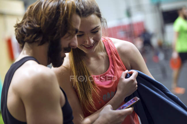 Весела жінка, дивлячись на інструктора, який переглядає смартфон у спортзалі — стокове фото