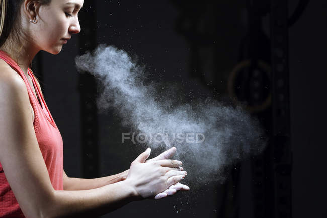 Sporty woman clapping hands with chalk powder on dark background. — Stock Photo