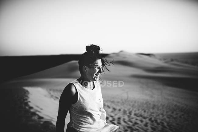 Веселая женщина стоит на песке и смотрит в сторону — стоковое фото