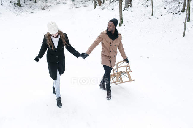 Feliz casal romântico com trenó andando na floresta — Fotografia de Stock