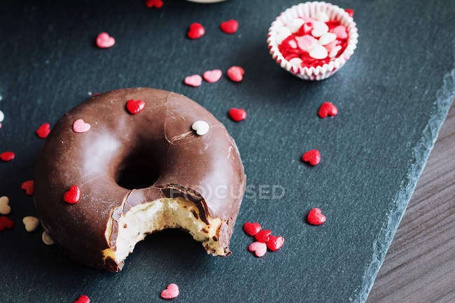 Donut de chocolate mordido con coberturas en la mesa - foto de stock
