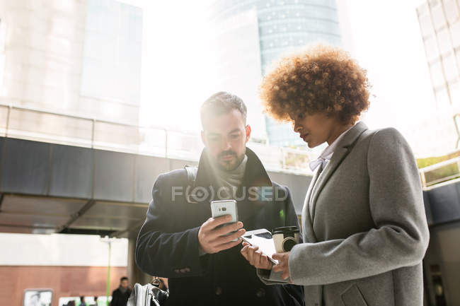 Стильна жінка дивиться на чоловіка, який переглядає смартфон — стокове фото