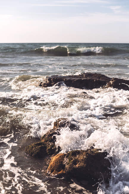 Coastal stones in surfing ocean waves on sunny day. — Stock Photo