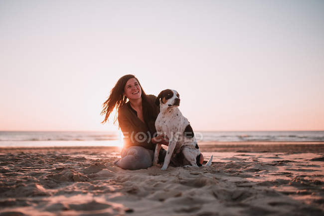 Mulher alegre com cão sentado na areia no dia ensolarado . — Fotografia de Stock