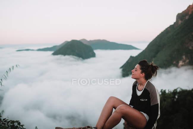 Brunette woman resting on picturesque background of mountains and clouds. — Stock Photo