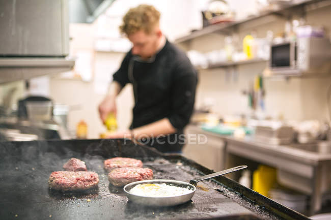 Patties and eggs frying on kitchen stove on background of blurred cook — Stock Photo
