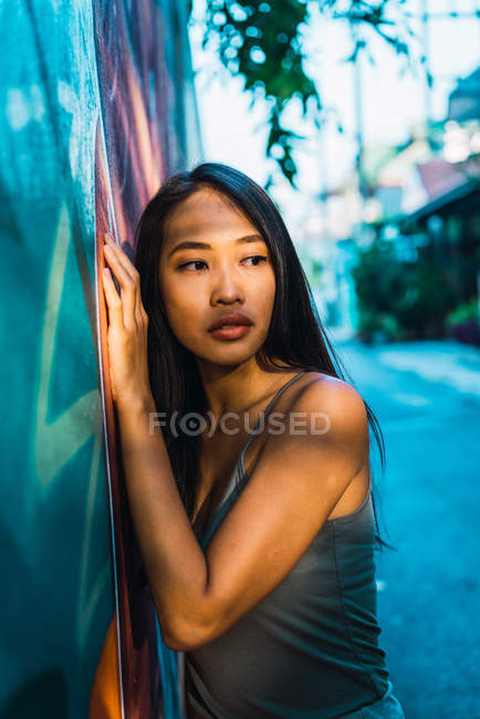 Mujer joven pensativa apoyada en la puerta azul y mirando hacia otro lado - foto de stock