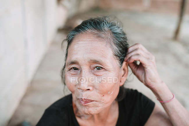 NONG KHIAW, LAOS: Mulher idosa ajustando o cabelo enquanto sentada na rua da aldeia
. — Fotografia de Stock