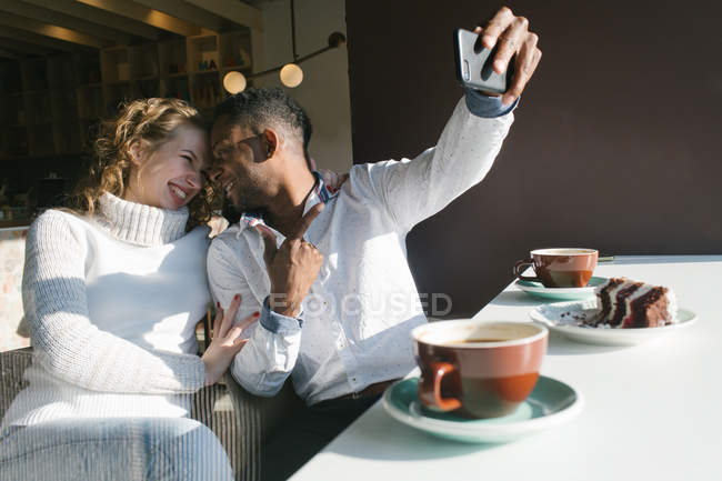 Cheerful couple taking selfie with smartphone in cafe — Stock Photo