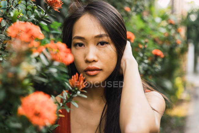 Sensual young woman posing at orange blooming bush and holding hair — Stock Photo