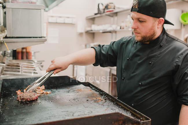 Koch dreht und kocht Patty mit Speck auf Herd — Stockfoto