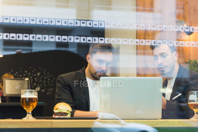 Empresarios navegando portátil detrás del vidrio de la cafetería - foto de stock