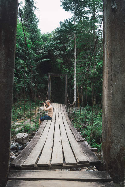 Мужчина без рубашки сидит на краю деревянного моста — стоковое фото
