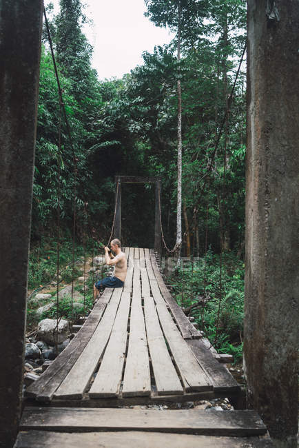 Shirtless fit man sitting on edge ofwooden bridge — Stock Photo