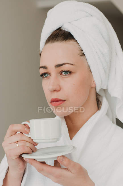 Продумана жінка в рушничку стоїть з керамічною чашкою і дивиться в сторону . — стокове фото