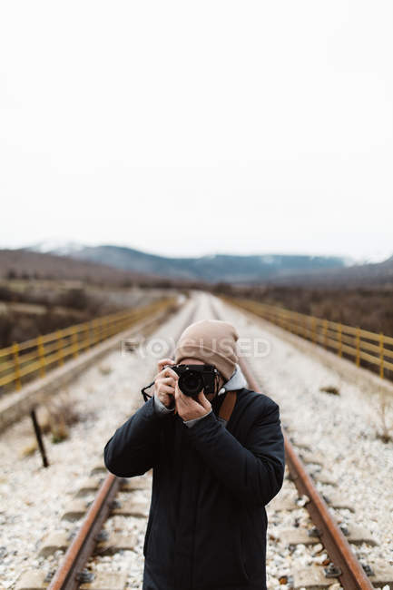 Неузнаваемый фотограф стоит на пустой железной дороге и целится камерой
. — стоковое фото