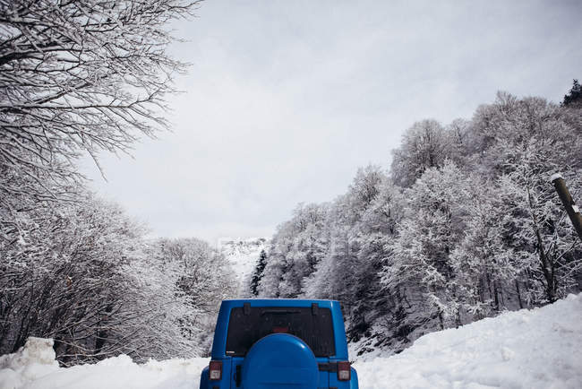 Обрезанное изображение синей машины, припаркованной на снежной дороге зимой . — стоковое фото