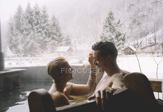 Casal amoroso sentado na banheira de mergulho exterior na natureza inverno . — Fotografia de Stock