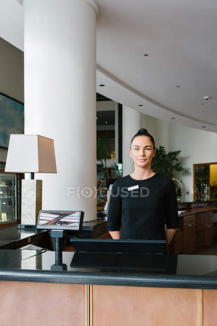 Hotelangestellte steht an der Rezeption und blickt in die Kamera — Stockfoto