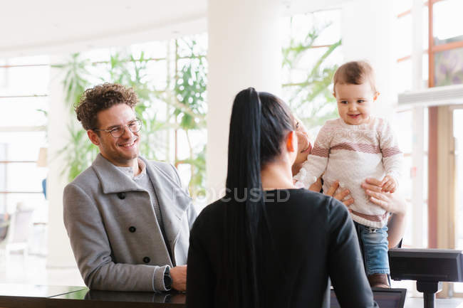 Joven familia con bebé en la recepción del hotel - foto de stock