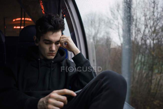 Задумчивый человек сидит и пользуется смартфоном в автобусе в дождливый день . — стоковое фото