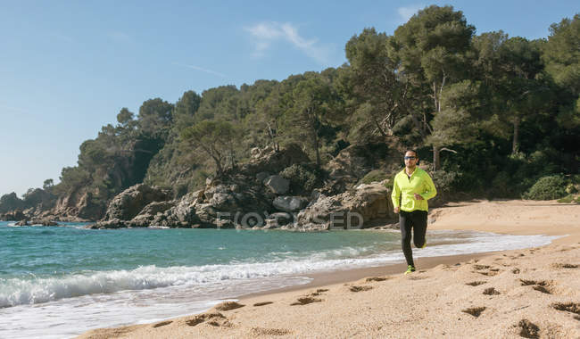 Чоловік біжить уздовж печатки на піщаному пляжі — стокове фото