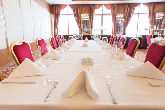 Interior of restaurant and big served table with red chairs. — Stock Photo