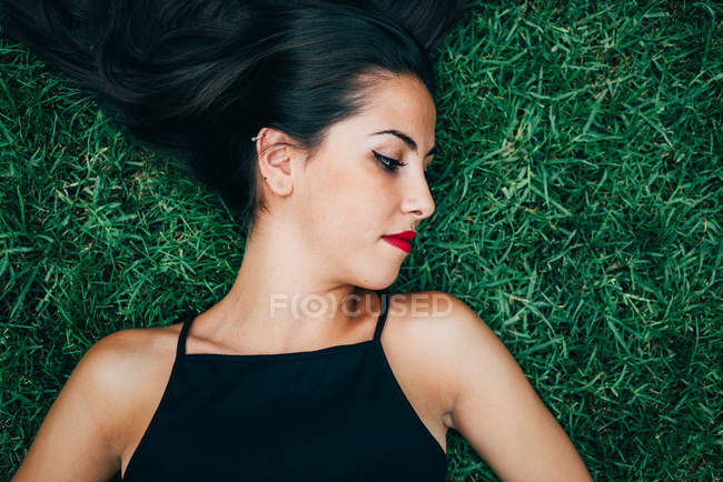 Mulher morena com lábios vermelhos deitado na grama — Fotografia de Stock