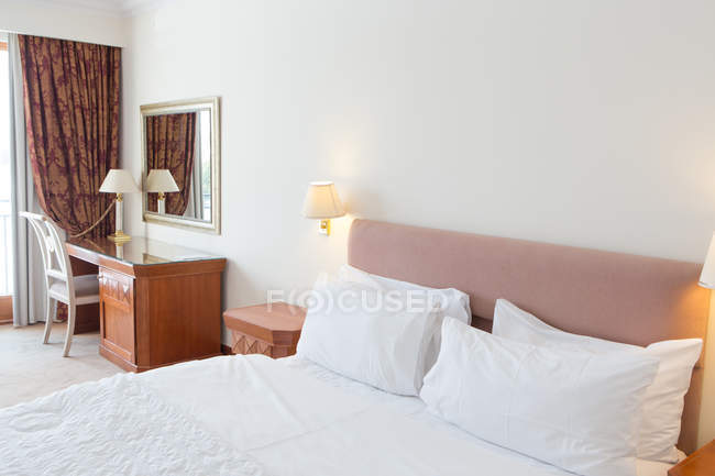 Interior of hotel room with white bed and wooden table. — Stock Photo