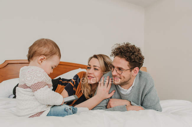 Alegre familia joven con niño en la cama - foto de stock