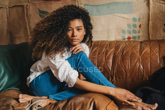 Stylische Frau sitzt auf Ledercouch und blickt in die Kamera. — Stockfoto