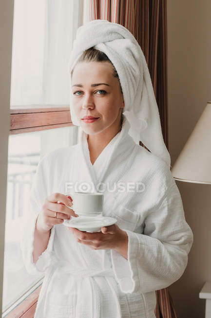 Nachdenkliche Frau, die nach dem Bad Kaffee trinkt und in die Kamera blickt — Stockfoto