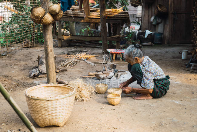 Лаос - 18 февраля 2018 года: Старшая женщина, сидящая во дворе и работающая — стоковое фото