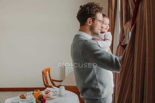 Fröhlicher Vater mit kleinem Kind steht am Fenster im Zimmer. — Stockfoto