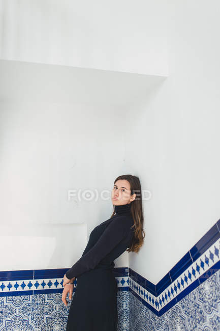 Mujer morena joven apoyada en la pared de azulejos azules en el hall de entrada . - foto de stock
